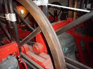 Close-up of church bells and wooden wheels with red metal frames inside a bell tower.