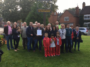 A group of people pose for a photo on grass near a "Community Council of Staffordshire" sign.