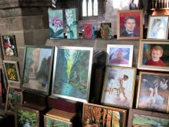 A display of various framed paintings, including portraits, landscapes, and flowers, inside a room with stone walls.