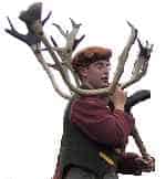 A person in historic clothing carries deer antlers on their shoulder.