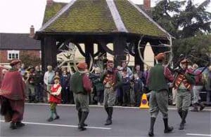 Morris dancers perform in costume before a crowd near a wooden market shelter.